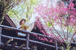 asiatisk kvinna reser naturen. resa slappna av. stående läser bok balkongen i huset. i sommar. foto