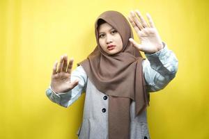 vacker asiatisk ung muslimsk kvinna med stoppskylt hand, avvisa tecken hand, förbudsskylt hand, närma sig inte handen, håll dig borta tecken hand, rör inte tecken hand, isolerad på gul bakgrund foto