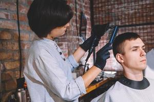 vacker kvinna frisör gör frisyr till ung man i frisörsalong. reklam och frisersalong koncept foto
