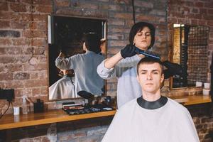 vacker kvinna frisör gör frisyr till ung man i frisörsalong. reklam och frisersalong koncept foto