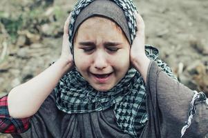 ett flyktingbarn i kriget, en muslimsk tjej med ett smutsigt ansikte på ruinerna, konceptet fred och krig, barnet gråter och väntar på hjälp. foto