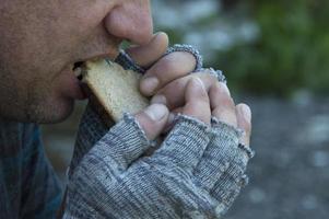 en hemlös, hungrig man äter girigt en bit bröd. fattigdom, arbetslöshet, hunger. porträtt. foto