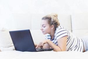 blond tjej sitter hemma i soffan med en bärbar dator och kommunicerar på internet. sociala nätverk. dejta. foto