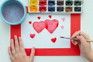 barnets hand ritar ett hjärta i akvarell på ett vitt ark. begreppet första kärlek. foto