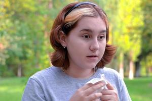 en ung flicka med allergier i en höstpark. nysande tjej med en servett i handen foto