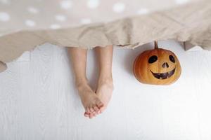 glad Halloween. benen på en liten flicka med pumpa ligger på golvet under bordet foto