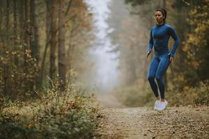 ung kvinna tar höjdhopp på skogsstigen på hösten foto