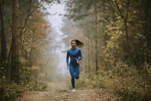 ung kvinna springer mot kameran på skogsstigen på hösten