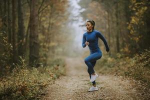 ung kvinna kör med motion på skogsstigen på hösten