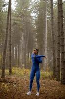 ung kvinna i blå träningsoverall sträcker sig innan träning i höstskogen foto