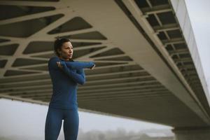 ung kvinna i blå träningsdräkt som sträcker sig innan träningen vid floden på höstmorgonen