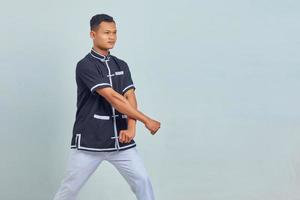 porträtt av asiatisk ung man som bär taekwondo kimono som visar boxergest över grå bakgrund foto