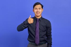 leende ung stilig affärsman och gör tummen upp på lila bakgrund foto