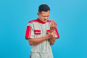 porträtt av ung asiatisk mekaniker som lider av smärta i händer och fingrar på blå bakgrund foto