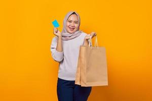 porträtt av glad asiatisk kvinna som håller shoppingväska och visar kreditkort över gul bakgrund foto