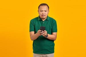 chockad stilig ung asiatisk man tittar på smartphoneskärmen isolerad på gul bakgrund foto
