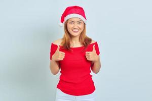 porträtt av vacker leende asiatisk kvinna som bär julklänning och visar tummen upp eller tecken på godkännande på vit bakgrund foto