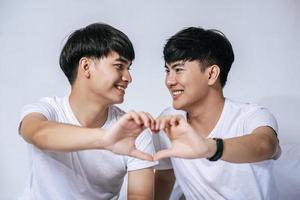 två kärleksfulla unga män tittar på varandra och gör en kärlekshandsymbol. foto