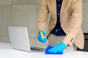 affärsman som bär mask och använder personligt desinfektionsmedel för att städa sitt kontor för att hålla hygienen. förebyggande under perioden med epidemi från coronavirus eller covid19. foto