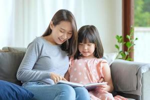 glad asiatisk mamma lär sin söta ungedotter att studera i vardagsrummet hemma foto