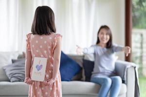 asiatisk söt tjej gömmer handgjort gratulationskort med jag älskar mamma ord att ge överraska sin mamma hemma foto
