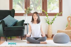 vacker asiatisk kvinna behåll lugnet och mediterar medan du övar yoga hemma för en hälsosam trendlivsstil foto
