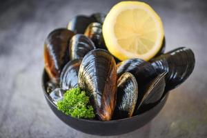 råa musslor med örter citron på skål och mörk bakgrund - färska skaldjursskaldjur på is i restaurangen eller till försäljning på marknaden musselmat foto