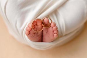 små fötter av ett nyfött barn med sina föräldrars vigselringar på fingrarna foto