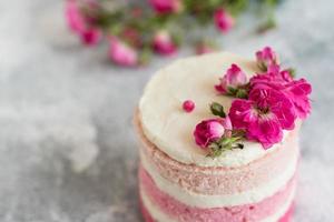 en liten tårta i vitt och rosa dekorerad med blommor och bär foto