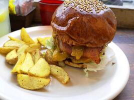 färsk street food nötkött hamburgare med brunt bröd, grönsaker, ost och såser och stekt pommes frites på vit platta. foto