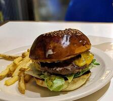 färsk street food nötkött hamburgare med brunt bröd, grönsaker, ost och såser och stekt pommes frites på vit platta. foto