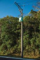 högspänningskraftstolpe med transformator och elektriska ledningar på gatan framför träd nära gramado. en söt europeisk influerad stad i södra Brasilien mycket eftertraktad av turister. foto