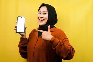 vacker ung asiatisk muslimsk kvinna som håller smartphone med vit eller tom skärm, marknadsför app, främjar något, isolerad, reklamkoncept foto