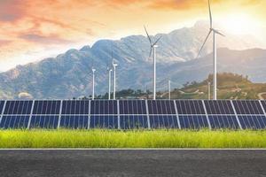 asfaltväg med solpaneler med vindkraftverk mot bergslandskap mot solnedgångshimmel, alternativ energikoncept