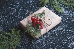 julklappsförpackning gjord av kraftpapper med snö på ett svart bord med grangrenar.