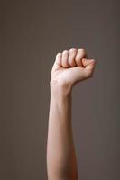 kvinnlig hand knuten till en näve på en grå bakgrund. gest att slåss, vinna eller protestera. mänsklig hand gester tecken isolerade. kvinnlig höjd arm presenterar populär gest. kopieringsutrymme foto