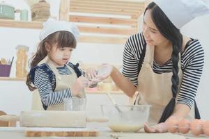glad och kärleksfull familjemamma och hennes dotter lagar mat tillsammans för att göra en tårta i köksrummet. fotodesign för familj, barn och glada människor koncept foto