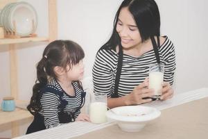 lycklig familj av asiatisk mamma dricker mjölk med sin söta dotter på morgonen. fotoserie av familj, barn och glada människor koncept. foto