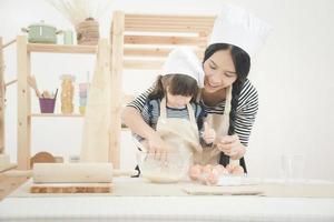 lycklig familj i köket. asiatisk mor och hennes dotter förbereder degen för att göra en cake.photo design för familj, barn och glada människor koncept. foto