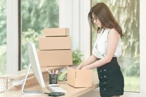 asiatisk entreprenör packar in produkten i lådan för sina kunder efter att ha fått beställning på hemmakontoret. konceptuellt för småföretag som startar eget företag och marknadsföring online. foto