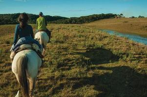 cambara do sul, Brasilien - 18 juli 2019. flicka och man rider häst i ett landskap av lantliga lågland som kallas pampas vid solnedgången nära cambara do sul. en lantlig stad med fantastiska naturliga turistattraktioner. foto