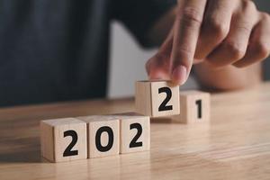 man hand sätter träkubblock för att ändra 2021 år till 2022 år på träbord med kopieringsutrymme. start på år 2022. gott nytt år koncept. foto