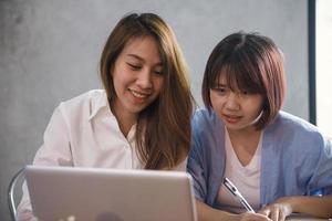 två unga affärskvinnor som sitter vid bordet i kafé. asiatiska kvinnor som använder bärbar dator och kopp kaffe. frilansare som arbetar på kafé. arbetar utanför kontorets livsstil. en-mot-en-möte. foto