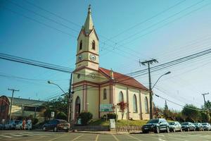 nova petropolis, brasilien - 20 juli 2019. liten kyrka med torn i gathörnet och människor på nova petropolis. en härlig lantlig stad grundad av tyska invandrare. foto