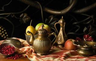 frukt och en metallkanna med skålar i orientalisk stil på bakgrund av dekorativ smidesprydnad. stilleben i orientalisk stil foto