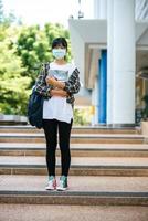 kvinnliga studenter bär masker, står i trappor och håller i böcker. foto