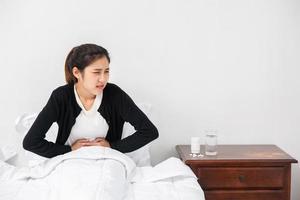 en kvinna som sitter i sängen med buksmärtor och trycker handen på magen. foto