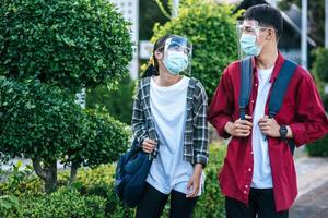 manliga och kvinnliga studenter bär ansiktskylning och masker går längs gångvägen foto