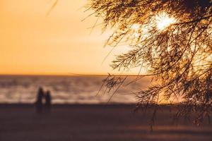 par som promenerar längs en ökenstrand vid solnedgången foto