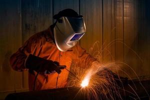 industriarbetare med säkerhetsutrustning och skyddsmasksvetsande stålkonstruktion i byggfabrik. foto
